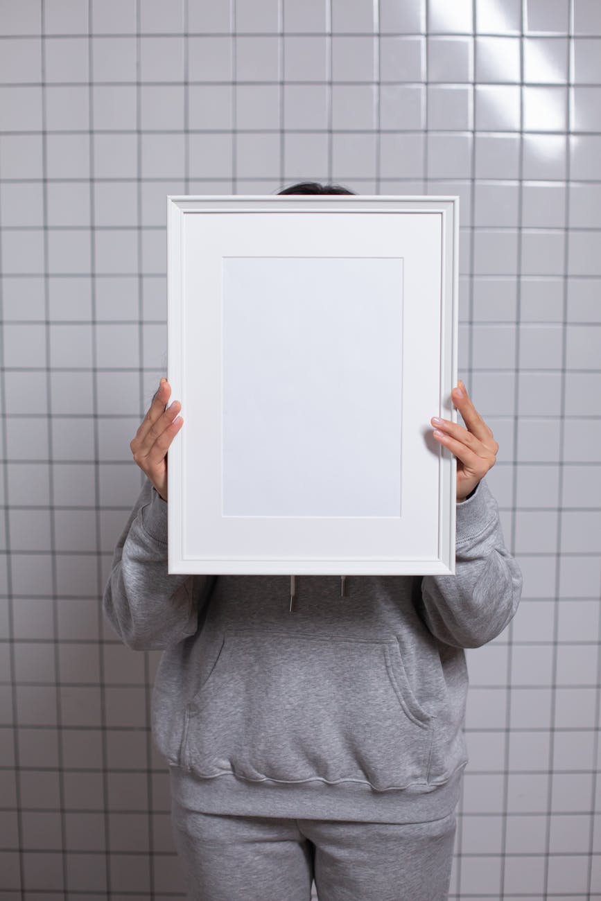 anonymous person covering face with empty white photo frame