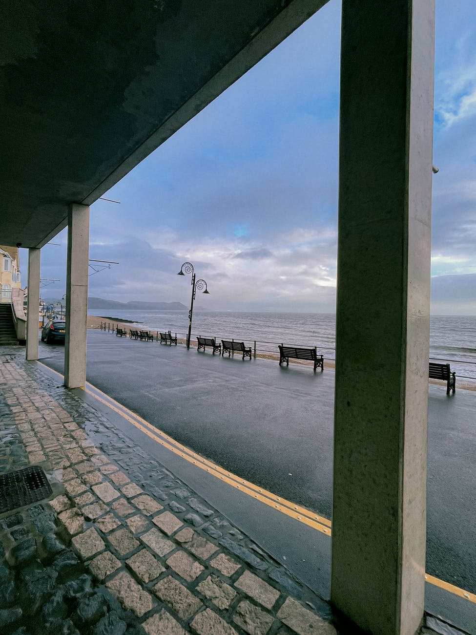 embankment with pillars near road with benches near sea
